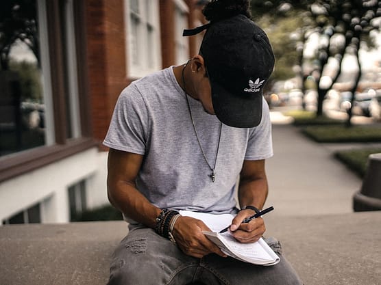 Photo by Brad Neathery person in black adidas cap sitting on bench writing on notebook